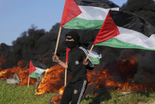 Demonštrant drží palestínske vlajky pri horiacich pneumatikách počas protestu proti razii izraelskej armády. FOTO: TASR/AP