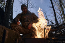 Ukrajinskí vojaci sa zohrievajú pri ohni na fronte v meste Bachmut v Doneckej oblasti na východe Ukrajiny v stredu 22. marca 2023. FOTO TASR/AP