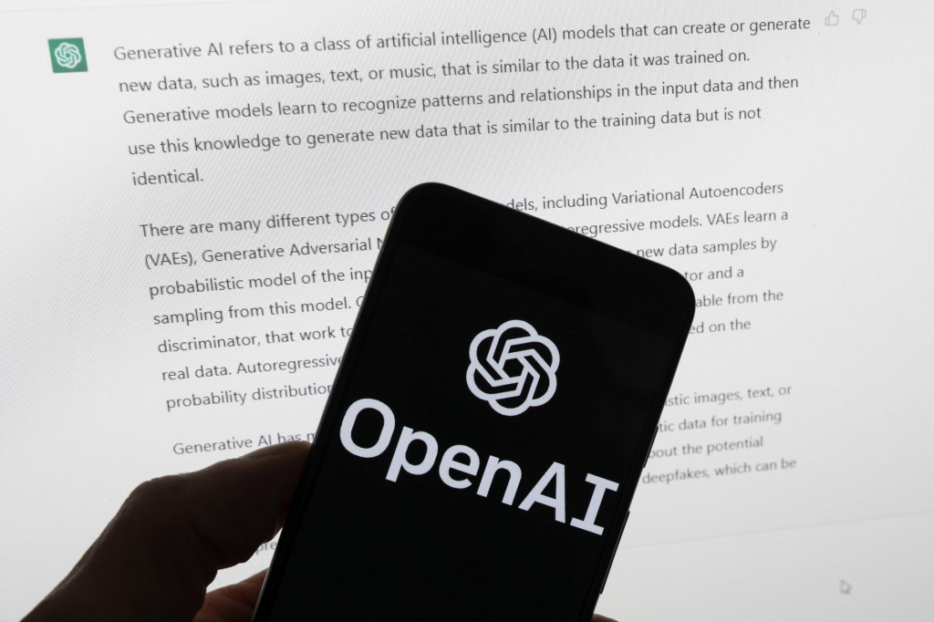 Logo americkej organizácie OpenAI svieti na displeji mobilného telefónu pred obrazovkou počítača, ktorá zobrazuje výstup z chatbotu ChatGPT. FOTO: TASR/AP