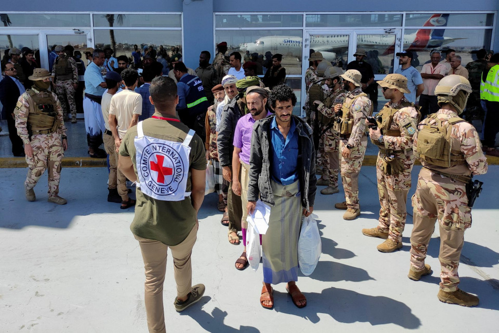 Prepustení väzni stoja a čakajú na nástup do lietadla prenajatého Medzinárodným výborom Červeného kríža na letisku v Adene. FOTO: Reuters