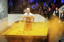 Ekologický aktivista vysypáva žltý prášok na stôl počas úvodného frejmu duelu medzi Robertom Milkinsom a Joeom Perrym na majstrovstvách sveta v snookri v sheffieldskom divadle Crucible. FOTO: TASR/AP