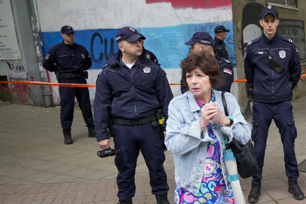 Žena stojí pred policajtmi, ktorí hliadkujú na ulici pred základnou školou v Belehrade. FOTO: TASR/AP