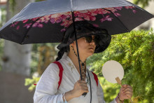 Žena kráča s dáždnikom a vejárom na osvieženie vo verejnom parku počas horúčav v Pekingu. FOTO: TASR/AP