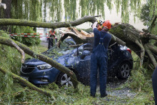 Hasiči odstraňujú polámané konáre stromov, ktoré spadli na zaparkované auto počas búrky v nemeckom meste Frankfurt. FOTO: TASR/AP