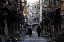 Ženy prechádzajú okolo poškodených budov v utečeneckom tábore na južnom okraji Damasku v Sýrii. FOTO: Reuters