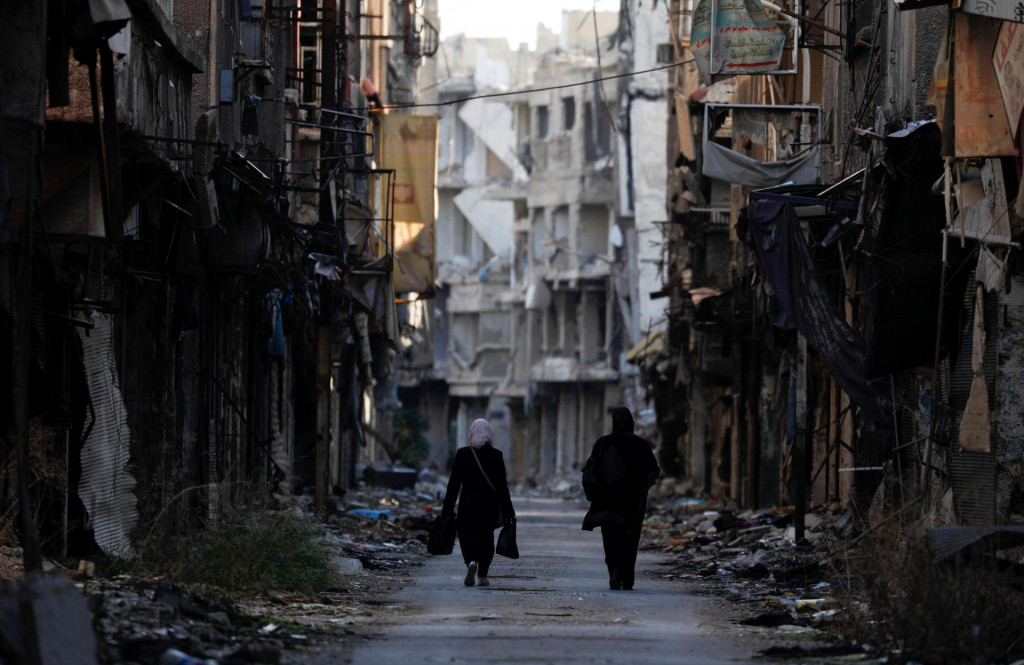Ženy prechádzajú okolo poškodených budov v utečeneckom tábore na južnom okraji Damasku v Sýrii. FOTO: Reuters