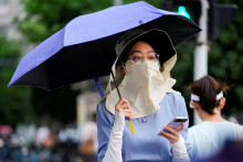 Žena kráča po ulici a chráni sa pred slnkom klobúkom, maskou a dáždnikom v Číne. FOTO: Reuters