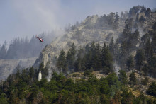Vrtuľník zhadzuje vodu na dym zo zhoreného lesa nad švajčiarskymi obcami Bitsch a Ried-Mörel. FOTO: TASR/AP