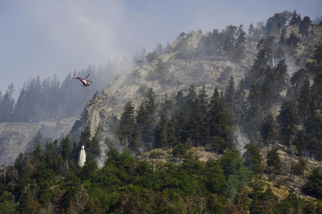 Vrtuľník zhadzuje vodu na dym zo zhoreného lesa nad švajčiarskymi obcami Bitsch a Ried-Mörel. FOTO: TASR/AP