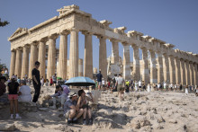 Turisti pijú vodu pod dáždnikom počas horúčav na Akropole v Aténach. FOTO: TASR/AP