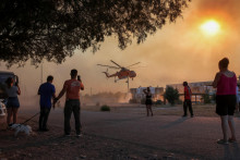 Ľudia sledujú hasičskú helikoptéru na gréckom ostrove Rodos. FOTO: Reuters