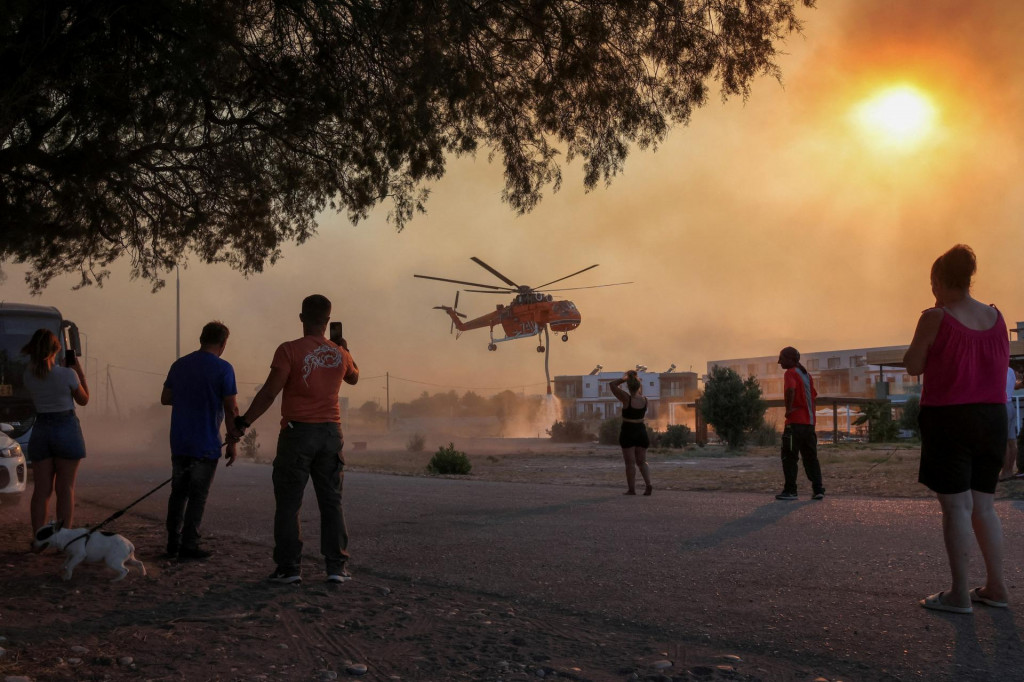 Ľudia sledujú hasičskú helikoptéru na gréckom ostrove Rodos. FOTO: Reuters
