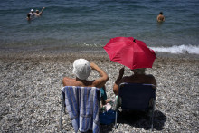 Žena sa chráni dáždnikom pred slnkom počas horúčav na pláži v meste západne od Atén. FOTO: TASR/AP