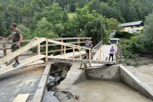 Ľudia kráčajú po moste po záplavách v meste Mežica na severe Slovinska. FOTO: TASR/STA