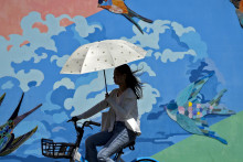 Cyklistka sa chráni dáždnikom počas horúčav v Pekingu v stredu 23. augusta 2023.