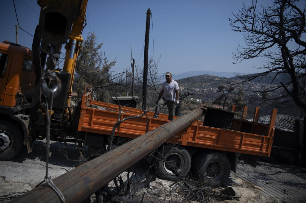 Pracovníci vymieňajú stĺp elektrického vedenia po lesnom požiari v mestečku Fyli na predmestí Atén. FOTO: TASR/AP