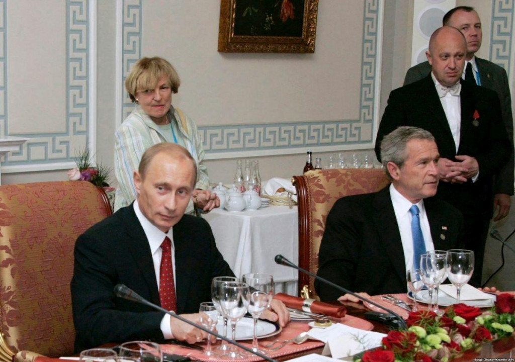Ruský prezident Vladimír Putin sa dňa 19. júla 2006 zúčastnil pracovnej večere spolu s americkým prezidentom Goergom Bushom mladším v Petrohrade, Jevgenij Prigožin – „Putinov kuchár“, stojí za nimi. FOTO: Profimedia