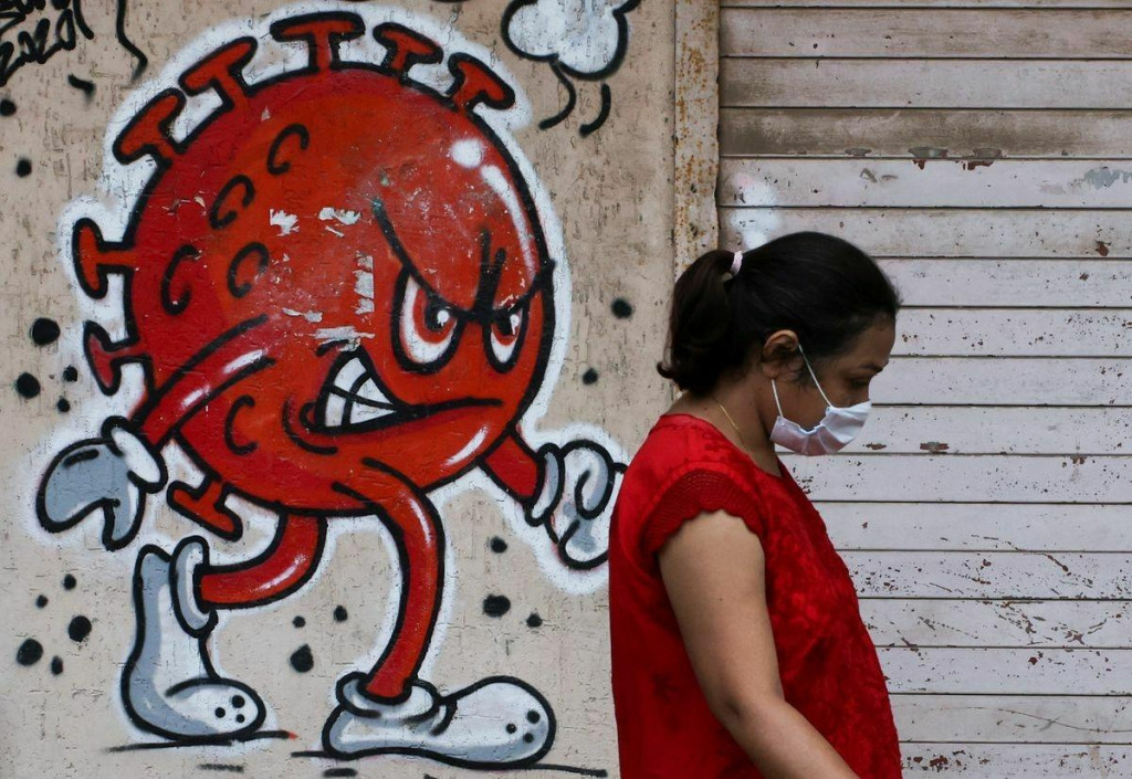 Žena prechádza okolo graffiti s tematikou koronavírusu.