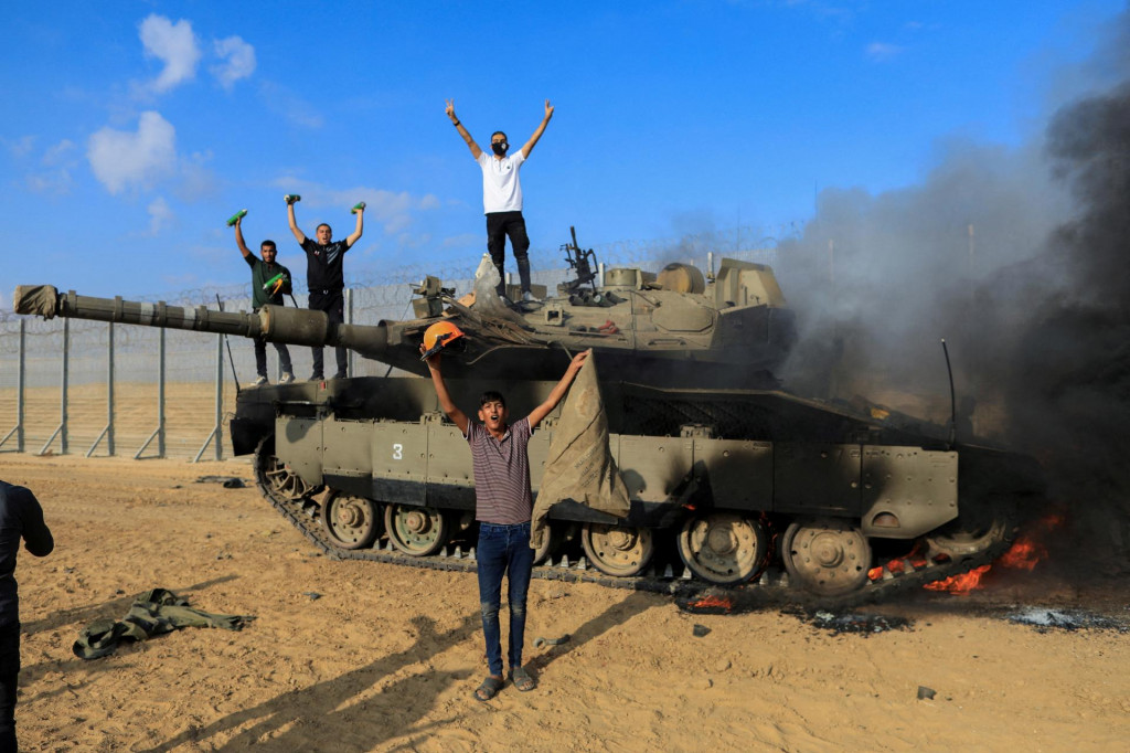 Palestínčania oslavujú, ako zhorí izraelské vojenské vozidlo po tom, čo ho zasiahli palestínski ozbrojenci, ktorí prenikli do oblastí južného Izraela. FOTO: Reuters