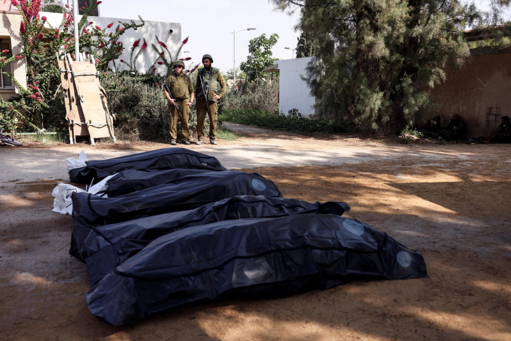 Izraelskí vojaci strážia telá obetí útoku po masovej infiltrácii ozbrojencov Hamasu z pásma Gazy v kibuci Kfar Aza v južnom Izraeli. FOTO: Reuters