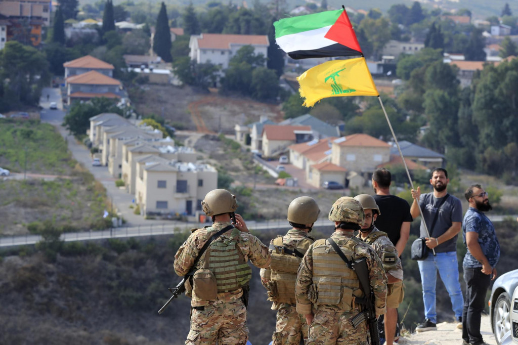 Libanonskí vojaci stoja na kopci v pohraničnej obci na juhu Libanonu, z ktorého je výhľad na severoizraelské mesto Metula. Muž vpravo máva vlajkou Palestíny a libanonského hnutia Hizballáh. FOTO: TASR/AP