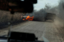Ukrajinskí vojaci prechádzajú okolo horiaceho auta zasiahnutého kamikadze dronom pred mestom Avdiivka v prvej línii. FOTO: Reuters