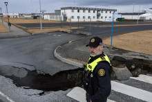 Policajt stojí pri trhline na ceste v rybárskom mestečku Grindavík, ktoré bolo evakuované v dôsledku sopečnej činnosti, na Islande. FOTO: Reuters