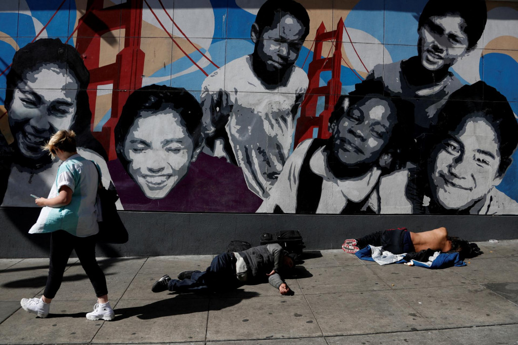 Žena prechádza okolo mužov bez domova ležiacich na chodníku v oblasti Tenderloin v San Franciscu. FOTO: Reuters