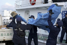 Členovia japonskej pobrežnej stráže nesú trosky, ktoré pravdepodobne pochádzajú z havarovaného amerického vojenského lietadla Osprey v prístave v Jakušime. FOTO: TASR/AP