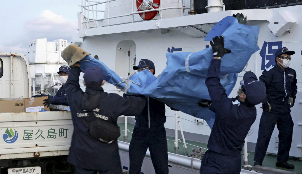 Členovia japonskej pobrežnej stráže nesú trosky, ktoré pravdepodobne pochádzajú z havarovaného amerického vojenského lietadla Osprey v prístave v Jakušime. FOTO: TASR/AP