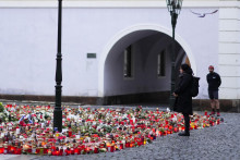 Ľudia sa pozerajú na kvety a sviečky položené pred budovou Filozofickej fakulty Univerzity Karlovej po štvrtkovej masovej streľbe. FOTO: TASR/AP