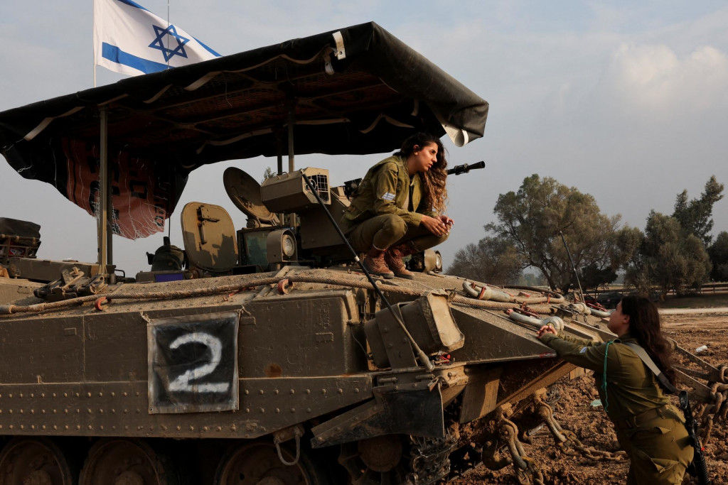 Izraelský vojak sa krčí na obrnenom transportéri. FOTO: Reuters