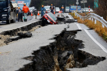 Robotníci opravujú cestu vedľa auta uviaznutého na rozbitej ceste po zemetrasení v Japonsku. FOTO: Reuters