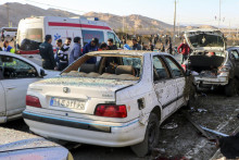 Ľudia stoja pri vraku auta po výbuchu v iránskom meste Kermán. FOTO: TASR/AP