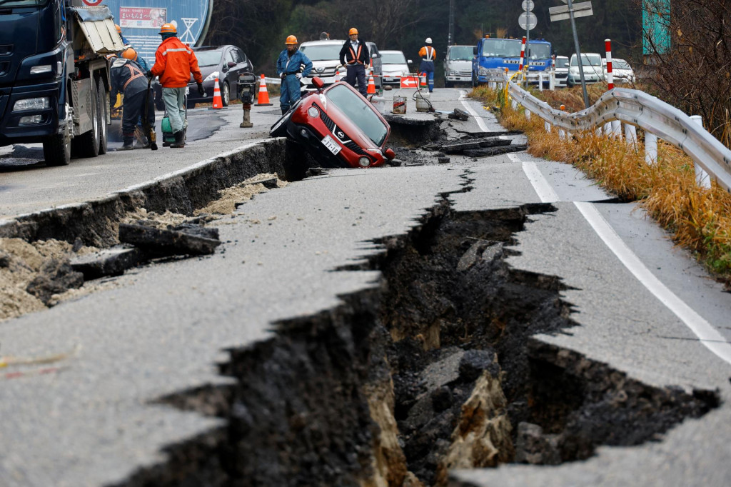 Robotníci opravujú cestu vedľa auta uviaznutého na rozbitej ceste po zemetrasení v Japonsku. FOTO: Reuters