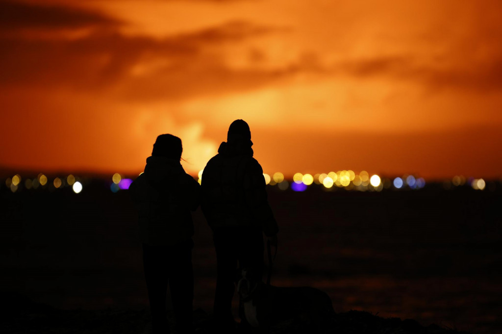 Ľudia sledujú nočnú oblohu z hlavného mesta Reykjavík po erupcii sopky, ku ktorej predtým došlo na polostrove Reykjanes na juhozápade Islandu v pondelok 18. decembra 2023. FOTO: TASR/AP
