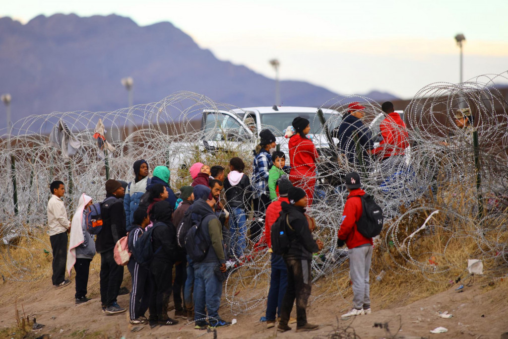 Migranti žiadajúci o azyl v Spojených štátoch sa pokúšajú prekročiť plot zo žiletkového drôtu nasadený na zabránenie prechodu migrantov. FOTO: REUTERS
