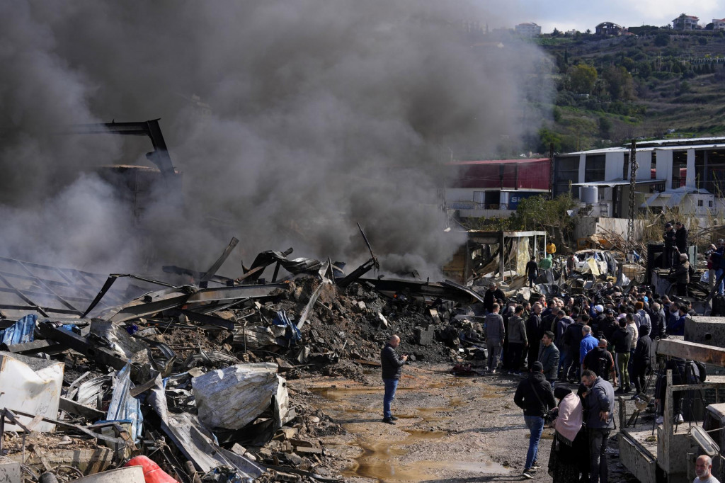 Ľudia sa zhromažďujú pri zničenom sklade po izraelskom leteckom útoku na priemyselnú zónu v prístavnom meste Ghazieh na juhu Libanonu. FOTO: TASR/AP