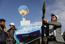 Stúpenec húsíovcov drží raketomet, zatiaľ čo ostatní nesú vystrihnutý transparent zobrazujúci nákladnú loď Galaxy Leader, ktorú hnutie zajalo počas prehliadky v rámci mobilizačnej kampane „ľudovej armády“. FOTO: Reuters