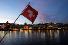 Švajčiarska vlajka počas východu slnka v Obchodnej a finančnej štvrti v Ženeve. FOTO: Reuters