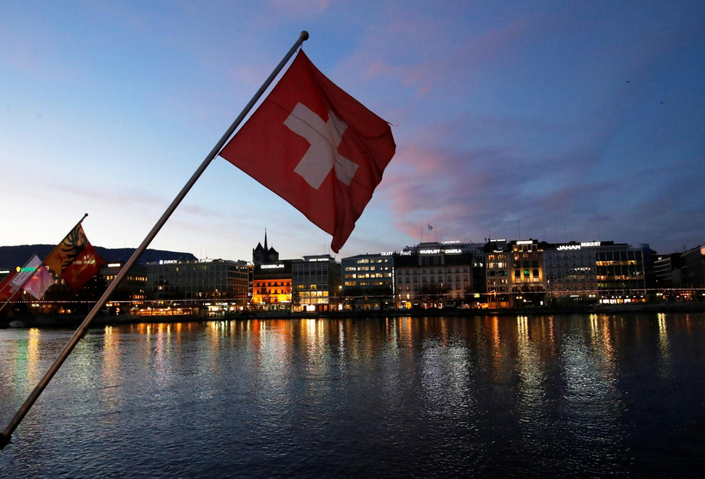Švajčiarska vlajka počas východu slnka v Obchodnej a finančnej štvrti v Ženeve. FOTO: Reuters