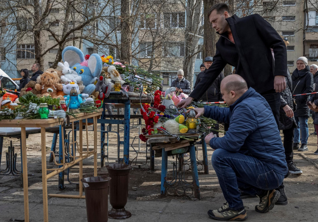 Ľudia zapaľujú sviečky a kladú kvety k provizórnemu pamätníku obetiam predošlého náletu bezpilotného lietadla, ktorý ťažko poškodil bytový dom v Odese. FOTO: Reuters
