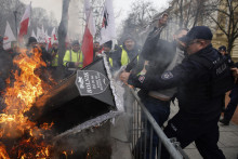 Policajt zastavuje demonštranta, ktorý hodil rakvu do ohňa na proteste farmárov vo Varšave. FOTO: TASR/AP
