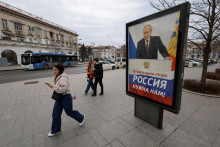 Obyvatelia krymského Sevastopoľa prechádzajú okolo predvolebného plagátu Vladimira Putina. FOTO: Reuters