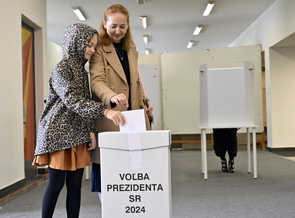 Žena s dieťaťom vhadzuje obálku s hlasovacím lístkom do volebnej schránky v prvom kole prezidentských volieb v novej volebnej miestnosti v športovej hale v Michalovciach. FOTO: TASR/Roman Hanc