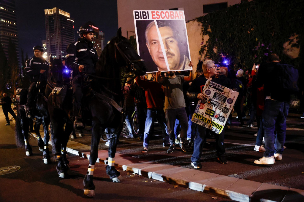 Osoba drží tabuľku s obrázkami izraelského premiéra Benjamina Netanjahua a Pabla Escobara, ako policajti na koňoch strážia oblasť počas protestu proti vláde izraelského premiéra a vyzývajú na prepustenie rukojemníkov unesených pri smrteľnom útoku zo 7. októbra. FOTO: Reuters