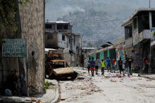 Ľudia prechádzajú okolo poškodeného auta v štvrti Carrefour Feuilles, ktorá bola opustená v dôsledku násilia gangov v Port-au-Prince. FOTO: Reuters