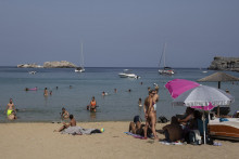 Turisti sa opaľujú na pláži na ostrove Rhodos na juhovýchode Grécka.  FOTO: TASR/AP