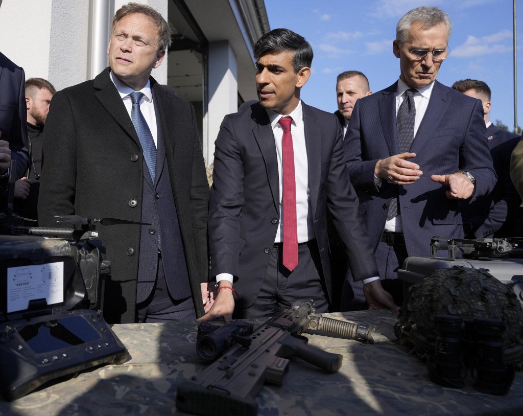 Generálny tajomník NATO Jens Stoltenberg (vpravo), britský premiér Rishi Sunak (uprostred) a britský minister obrany Grant Shapps (vľavo) sa pozerajú na zbrane počas ich návštevy základne prvej varšavskej obrnenej brigády vo Varšave. FOTO: TASR/AP