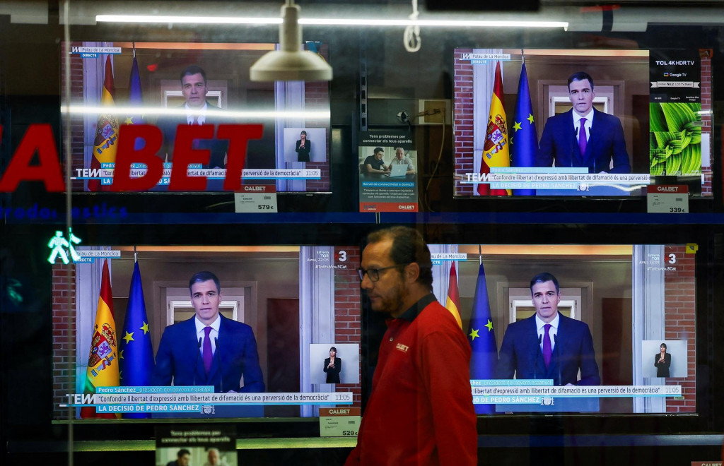 Osoba kráča vedľa televízorov, ktoré vysielajú vyhlásenie španielskeho premiéra Pedra Sáncheza. FOTO: Reuters
